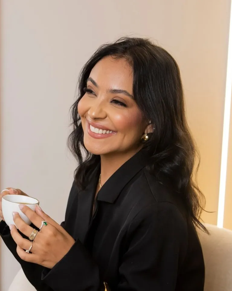 Dra. Alexia Rezende sorrindo, de blazer preto, segurando uma xícara no consultório